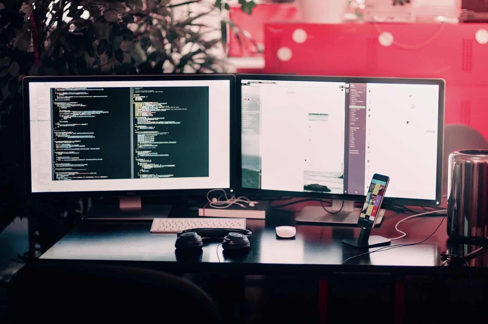 Two computer screens, 1 mobile phone and headphone on a desk